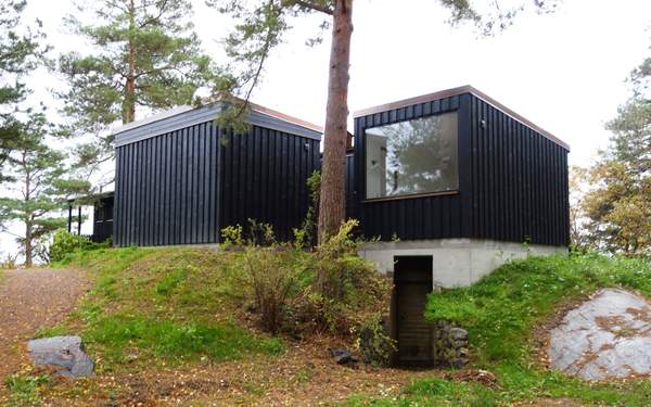 Ett litet hus i Arkösund i svart trä, kvadratiskt format, uppe på en kulle.