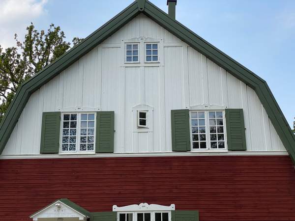 Äldre vitt trähus i Brokind med flera små fönster med gröna fönsterluckor.