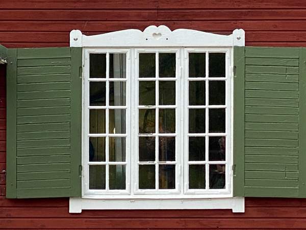 Ett fönster med vita ramar och gröna fönsterluckor i Brokind.