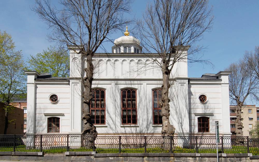 En vacker synagoga i Norrköping bakom två stora träd.