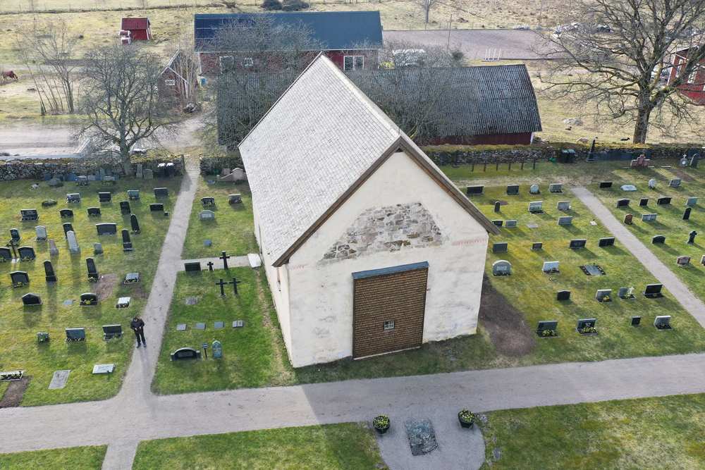 Vitt tegelhus vid Dädesjö gamla kyrka omgivet av gravar