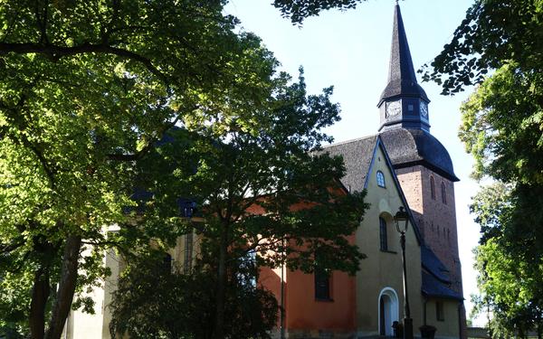 Fors kyrka med flera torn, bakom ett par grönskande träd.