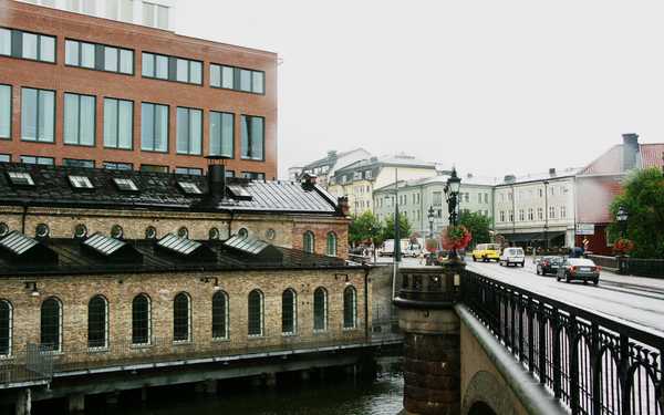 Campus Norrköpings byggnader, en ljus och en mörk intill vatten med en bro över där bilar kör.