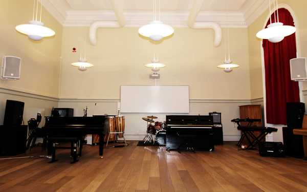 De Geergymnasiets musikssal med piano, trummor och en whiteboard tavla.