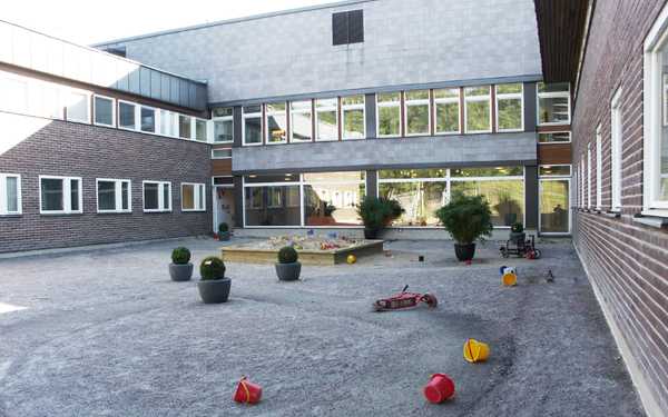 Erlaskolan med en sandlåda och leksaker på gården: en cykel och flera gula och röda bollar.