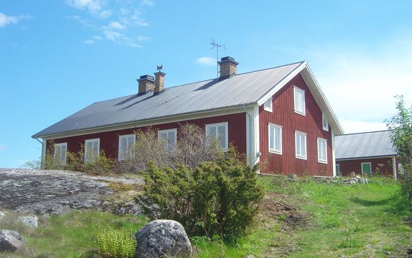 Mysiga röda byggnader i Häradsskär med vita knutar på en kulle i naturen.