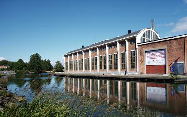 En lång tegelbyggnad i Gamla Motala verkstad med kupat tak intill vatten.