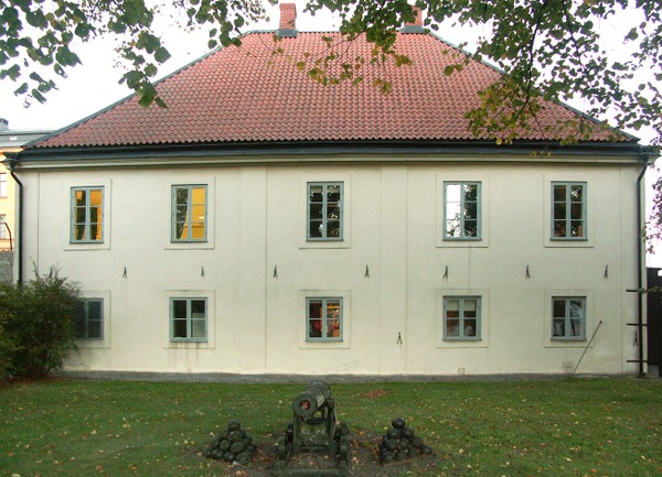 Tygkontoret i Karlskrona som är en beige byggnad med gröna fönsterkarmar och takpannor av tegel. Det står en kanon framför byggnaden på bilden.