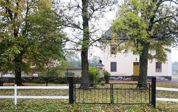 Vitt/beige hus med flera stora träd framför på Åkerholm.