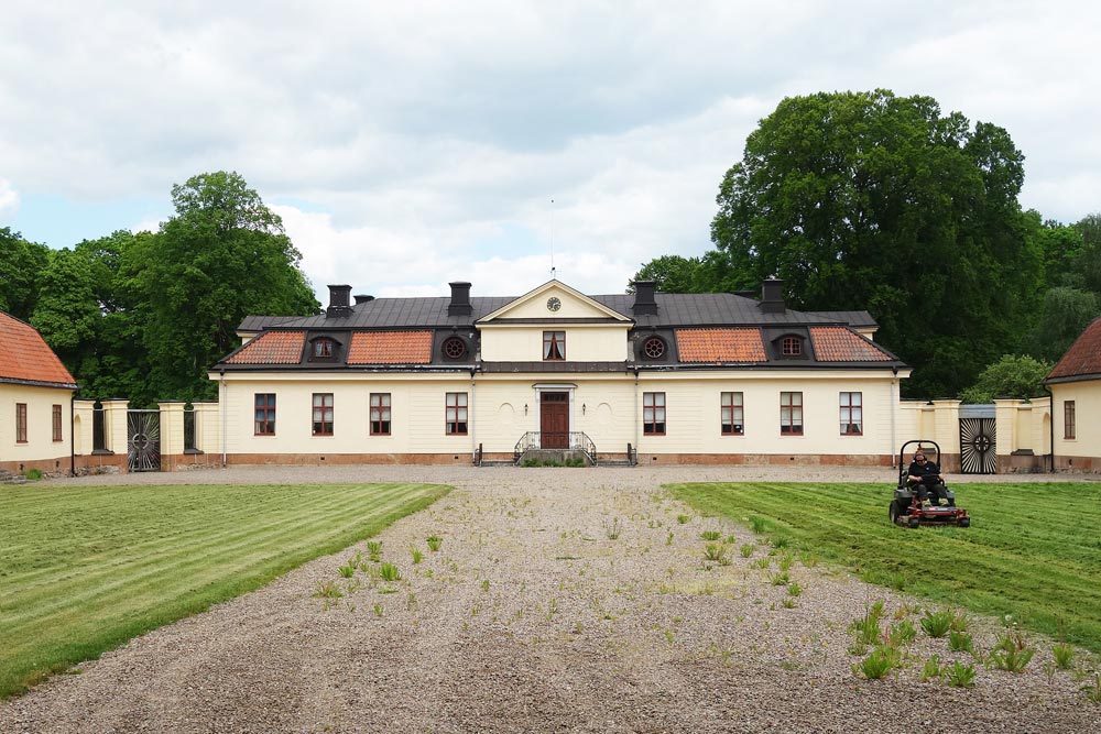 Lambohov slott med gräsmatta, någok klipper gräset.