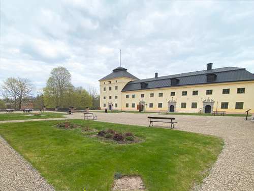 Löfstad slott i beige färg och många fönster med en grön gräsmatta framför.