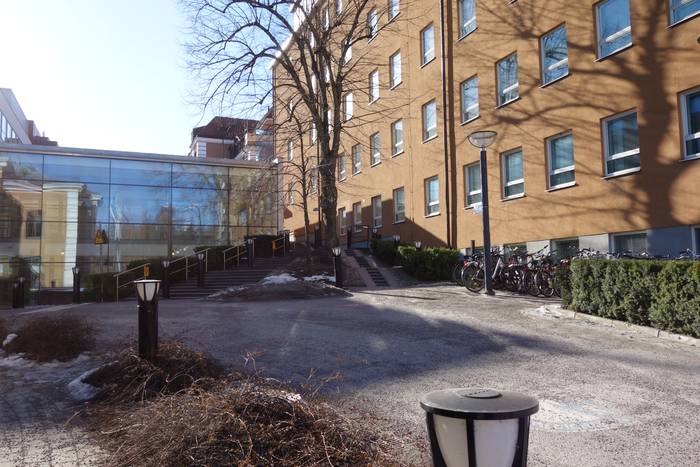 Grusig gångväg upp mot en gul byggnad med en byggnadsdel i glas vid Universitetssjukhuset i Linköping